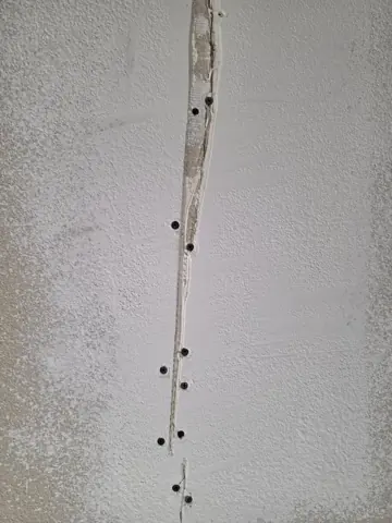 Additional screws securing drywall along the opened crack