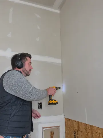 Dan fastening a sheet of drywall with a screw gun